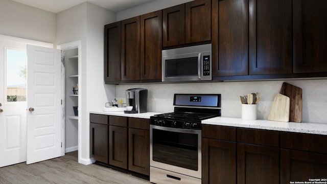 kitchen featuring backsplash, dark brown cabinetry, light wood-type flooring, and stainless steel appliances