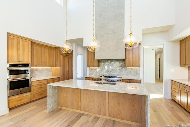 kitchen featuring double oven, light wood-style flooring, a sink, a towering ceiling, and light stone countertops