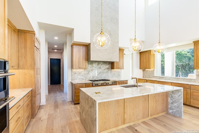 kitchen with a high ceiling, decorative backsplash, a kitchen island with sink, a sink, and light wood-type flooring