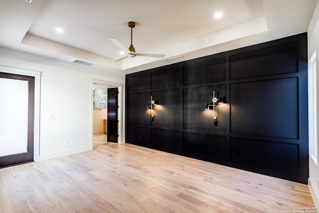 unfurnished bedroom with light wood finished floors, visible vents, a raised ceiling, and a decorative wall