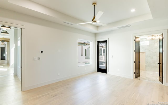 empty room featuring a tray ceiling, visible vents, light wood-style flooring, a ceiling fan, and baseboards