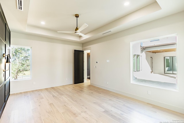 spare room featuring a tray ceiling, recessed lighting, light wood-style floors, a ceiling fan, and baseboards