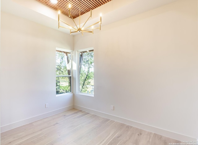 spare room featuring light wood-type flooring, baseboards, and a notable chandelier