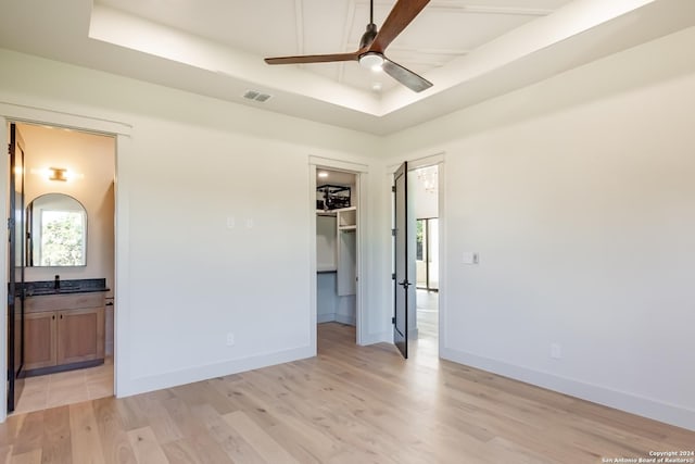 unfurnished bedroom featuring light wood-type flooring, a tray ceiling, a spacious closet, and baseboards