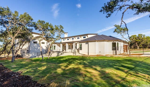 back of house with a lawn, a chimney, fence, and stucco siding