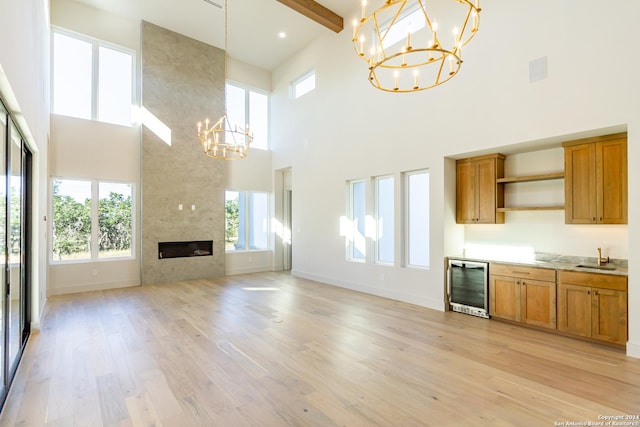 unfurnished living room featuring a chandelier, wine cooler, a large fireplace, baseboards, and light wood-style floors