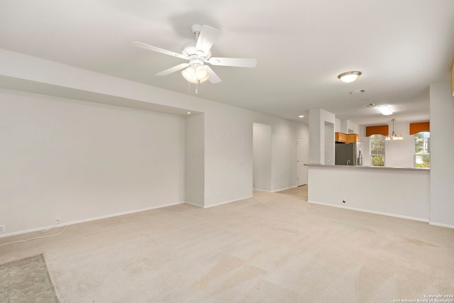 unfurnished living room featuring light carpet and ceiling fan with notable chandelier