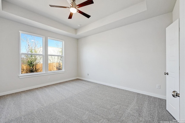 carpeted empty room with baseboards, a tray ceiling, and ceiling fan