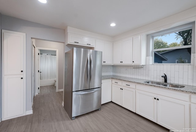 kitchen with white cabinetry, sink, light stone countertops, stainless steel fridge, and light hardwood / wood-style floors