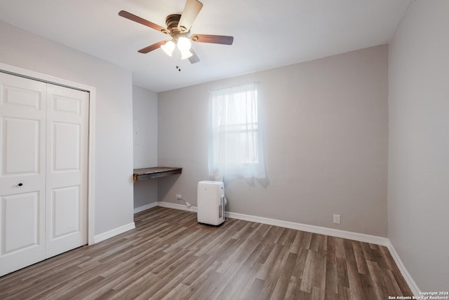 unfurnished bedroom with ceiling fan, built in desk, light wood-type flooring, and a closet