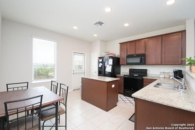 kitchen featuring sink, a center island, light tile patterned floors, black appliances, and light stone countertops