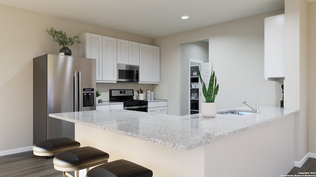 kitchen featuring kitchen peninsula, light stone counters, stainless steel appliances, sink, and white cabinets