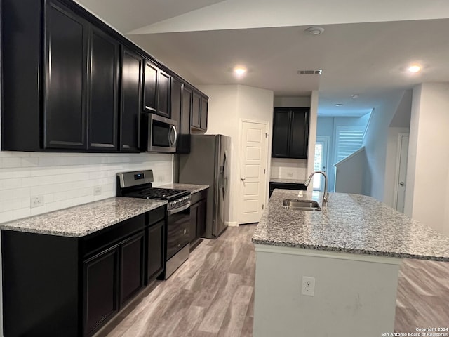 kitchen featuring appliances with stainless steel finishes, backsplash, sink, light hardwood / wood-style floors, and an island with sink