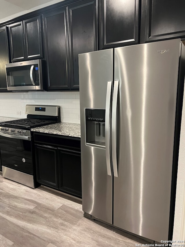 kitchen with decorative backsplash, appliances with stainless steel finishes, light hardwood / wood-style floors, and light stone countertops