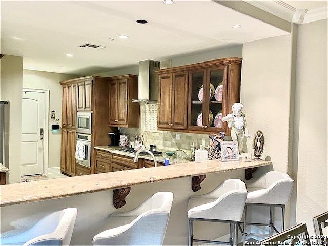 kitchen with wall chimney exhaust hood, stainless steel appliances, a kitchen breakfast bar, kitchen peninsula, and decorative backsplash