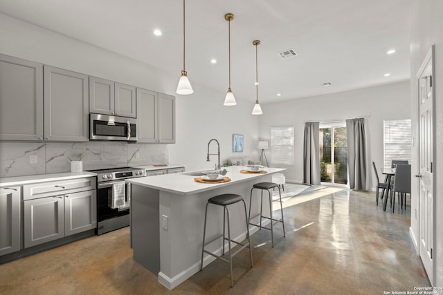 kitchen with backsplash, sink, an island with sink, appliances with stainless steel finishes, and a kitchen bar