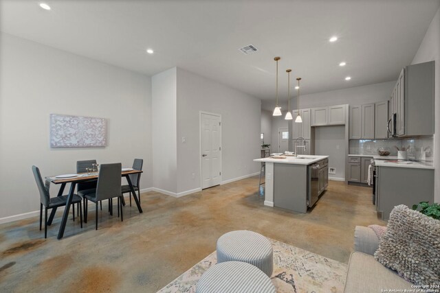 kitchen featuring tasteful backsplash, sink, gray cabinets, hanging light fixtures, and an island with sink