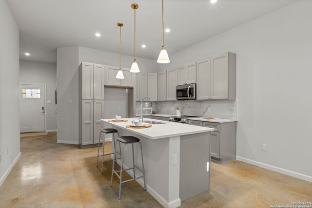 kitchen featuring stainless steel appliances, sink, a center island with sink, gray cabinets, and hanging light fixtures