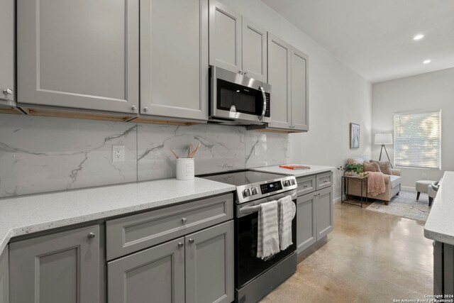 kitchen featuring gray cabinets, decorative backsplash, light stone countertops, and appliances with stainless steel finishes