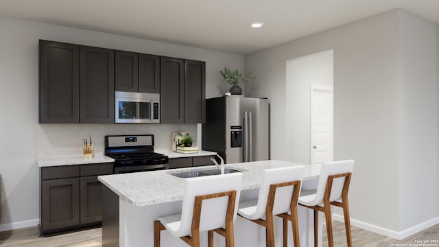 kitchen with a center island with sink, sink, light wood-type flooring, appliances with stainless steel finishes, and a kitchen bar