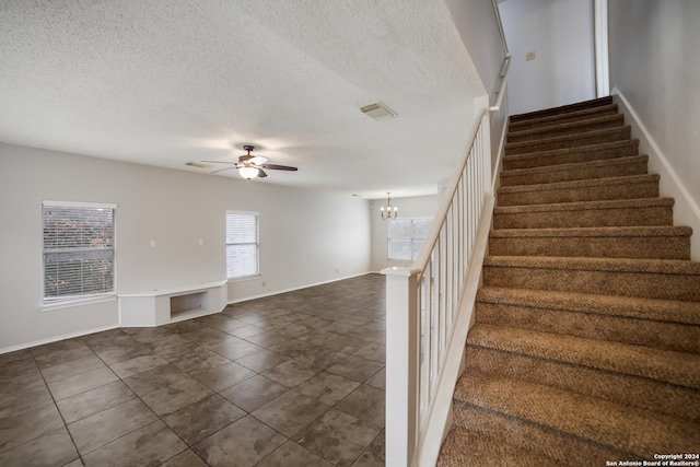 stairs with a textured ceiling, tile patterned flooring, and ceiling fan with notable chandelier