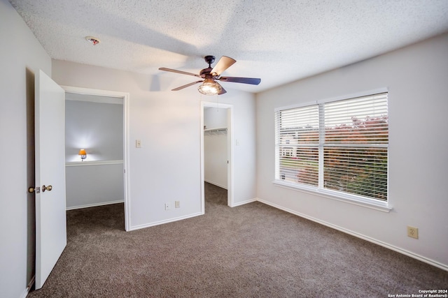 unfurnished bedroom featuring a walk in closet, dark carpet, a textured ceiling, ceiling fan, and a closet