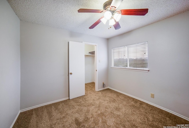 unfurnished bedroom featuring light carpet, a textured ceiling, a spacious closet, and ceiling fan