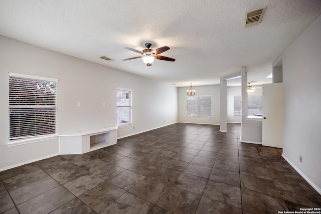 unfurnished living room featuring ceiling fan with notable chandelier, a textured ceiling, dark tile patterned floors, and a healthy amount of sunlight