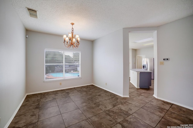 unfurnished room with dark tile patterned floors, a textured ceiling, and an inviting chandelier