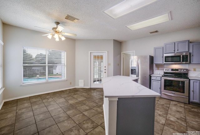 kitchen with appliances with stainless steel finishes, a textured ceiling, gray cabinets, and a kitchen island