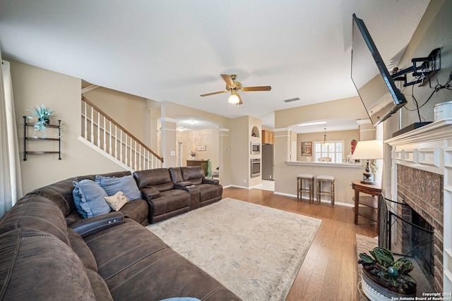 living room with ceiling fan, light hardwood / wood-style floors, a fireplace, and decorative columns