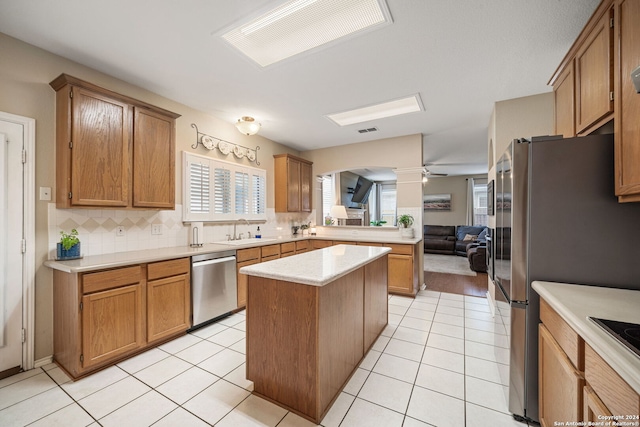 kitchen with decorative backsplash, appliances with stainless steel finishes, ceiling fan, sink, and a kitchen island