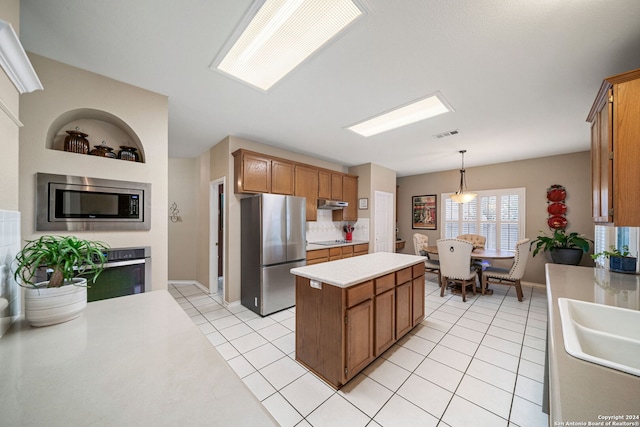 kitchen featuring stainless steel appliances, sink, a kitchen island, hanging light fixtures, and light tile patterned flooring