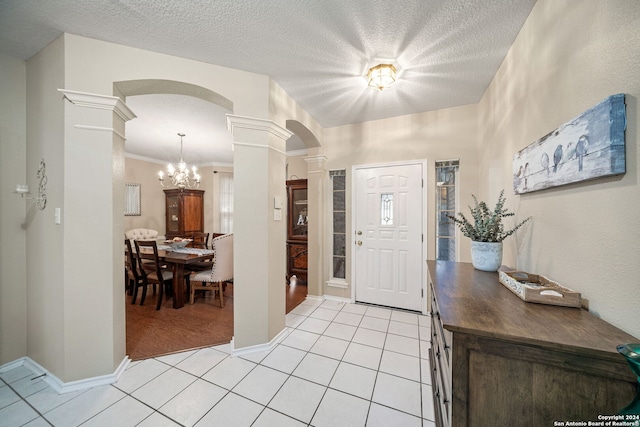 foyer featuring light wood-type flooring, decorative columns, a textured ceiling, crown molding, and a chandelier