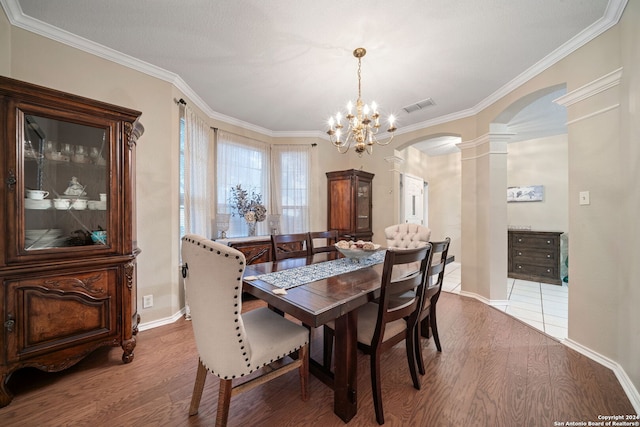 dining space featuring hardwood / wood-style floors, decorative columns, an inviting chandelier, and crown molding