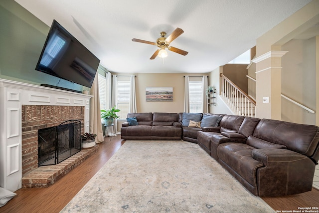 living room featuring a wealth of natural light, ceiling fan, wood-type flooring, and a brick fireplace