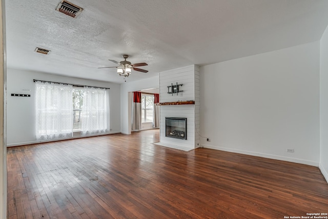 unfurnished living room with dark hardwood / wood-style floors, a large fireplace, a textured ceiling, and ceiling fan