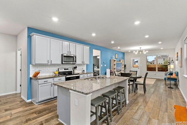 kitchen with a center island with sink, white cabinets, sink, light wood-type flooring, and appliances with stainless steel finishes