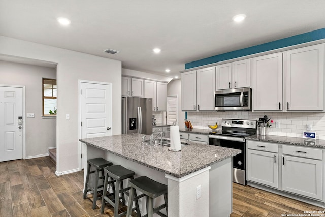 kitchen featuring a center island with sink, stone counters, dark hardwood / wood-style flooring, and appliances with stainless steel finishes