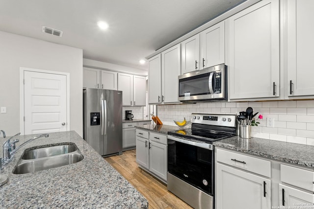 kitchen with sink, light stone countertops, light wood-type flooring, tasteful backsplash, and stainless steel appliances