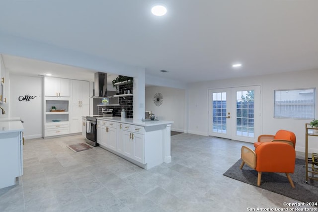 kitchen featuring stainless steel electric stove, white cabinets, wall chimney range hood, and french doors