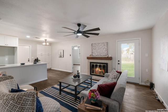 living room with a textured ceiling, a fireplace, dark hardwood / wood-style flooring, and ceiling fan with notable chandelier