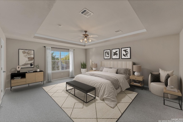 bedroom featuring a raised ceiling, ceiling fan, and light carpet