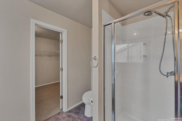 bathroom with tile patterned flooring, a textured ceiling, toilet, and a shower with door