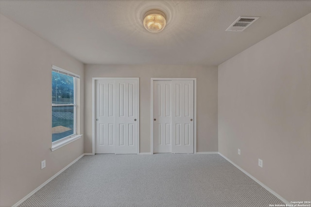 unfurnished bedroom with carpet, two closets, and multiple windows