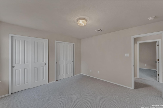 unfurnished bedroom featuring light colored carpet and multiple closets