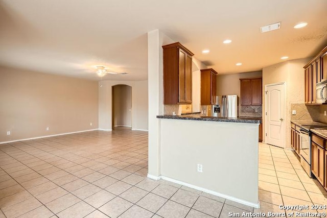 kitchen featuring ceiling fan, dark stone counters, decorative backsplash, light tile patterned floors, and appliances with stainless steel finishes