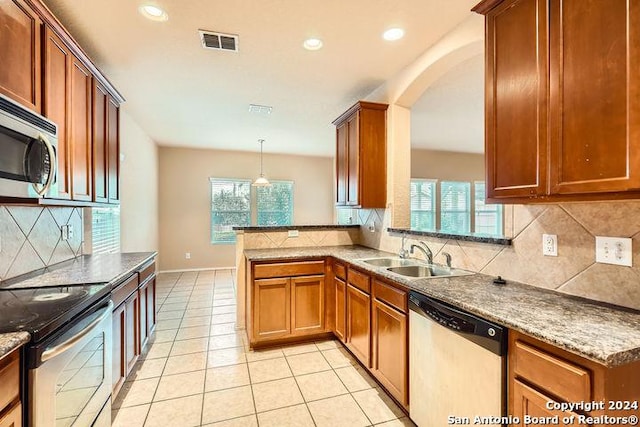 kitchen featuring kitchen peninsula, appliances with stainless steel finishes, backsplash, sink, and hanging light fixtures