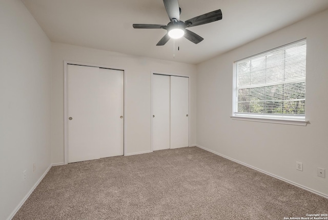 unfurnished bedroom featuring multiple closets, light carpet, and ceiling fan