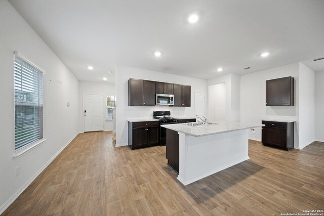 kitchen featuring dark brown cabinets, gas stove, a kitchen island with sink, sink, and light hardwood / wood-style floors